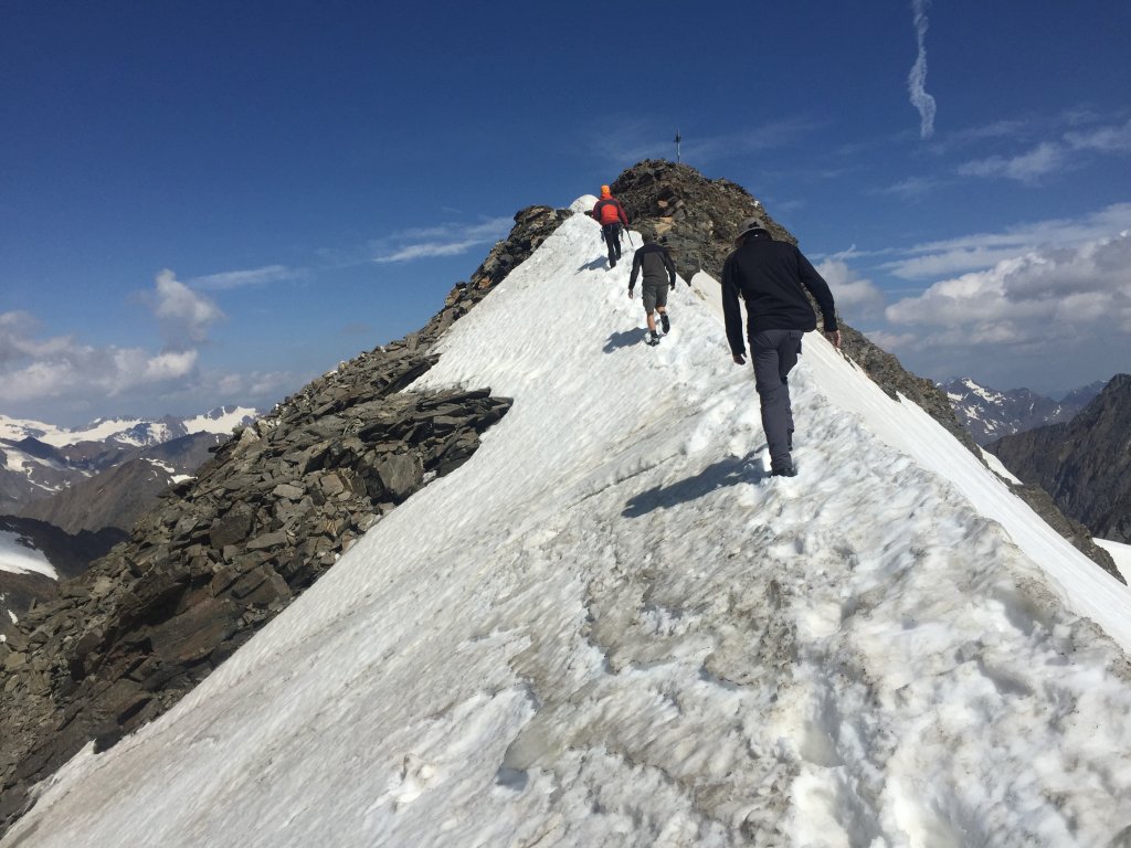 3 Wanderer erklimmen den Gipfel über eine Scheefeld